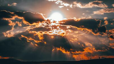 De zon schijnt door de wolken boven een heuvelig landschap