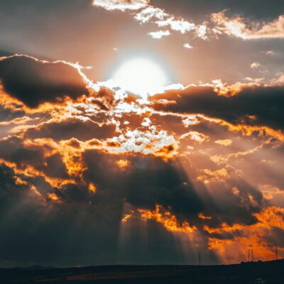 De zon schijnt door de wolken boven een heuvelig landschap